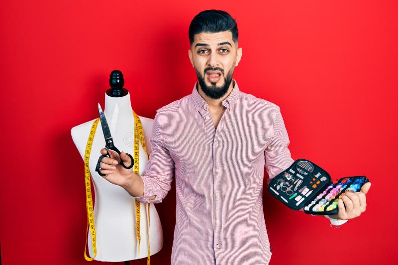 Handsome tailor man with beard holding sew kit and scissors in shock face, looking skeptical and sarcastic, surprised with open royalty free stock photos