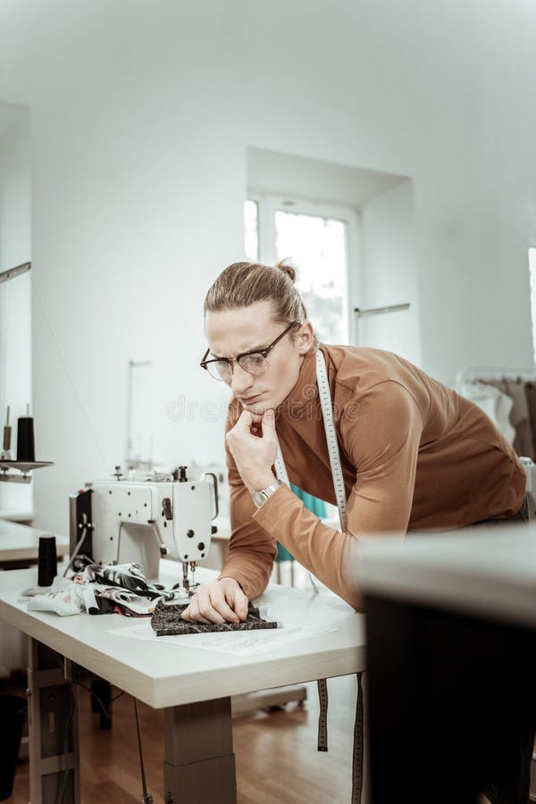 Handsome tall fashion dressmaker in a brown garment looking attentive