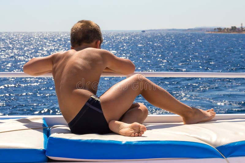 Handsome tanned boy looking to the blue sea from yacht board