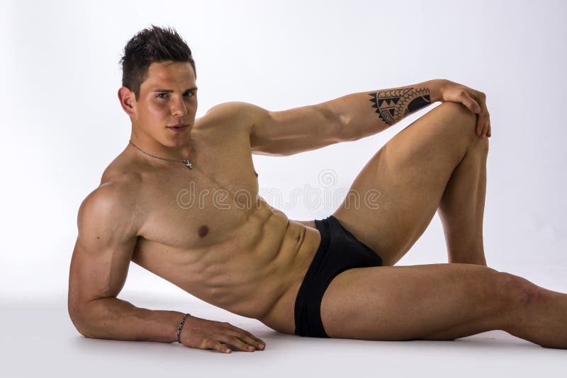 Handsome young bodybuilder laying down on the floor, showing ripped abs, mu...