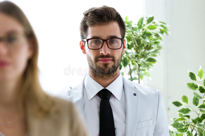 Handsome young businessman with his partner looking at camera in a hallway of they company.