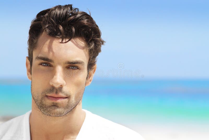 Bel giovane uomo casual top bianco contro luminosa spiaggia di sfondo.