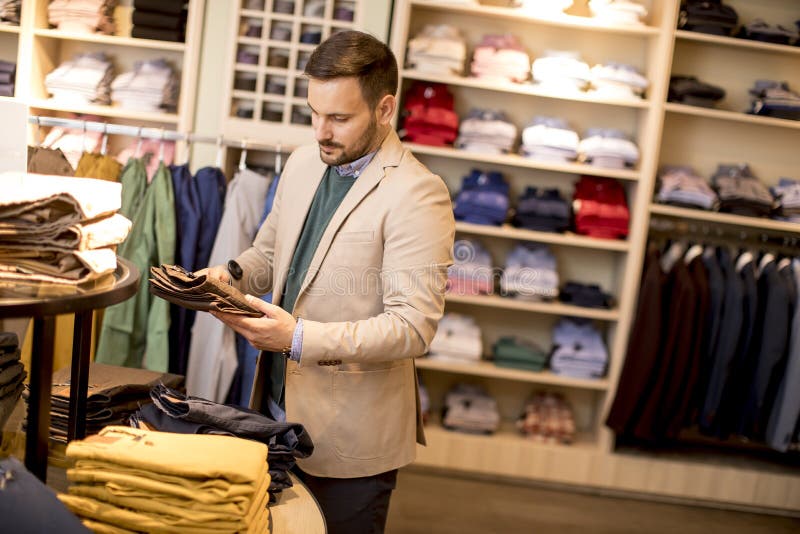 Handsome young man buying trousers in fashion store stock photos