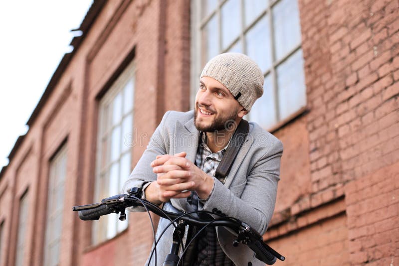 Handsome young man in grey coat and hat standing with his bicycle royalty free stock image Handsome young man in grey coat and hat standing with his bicycle royalty free stock image