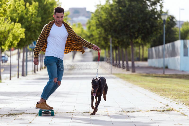 Portrait of handsome young man with his dog skateboarding in the park.