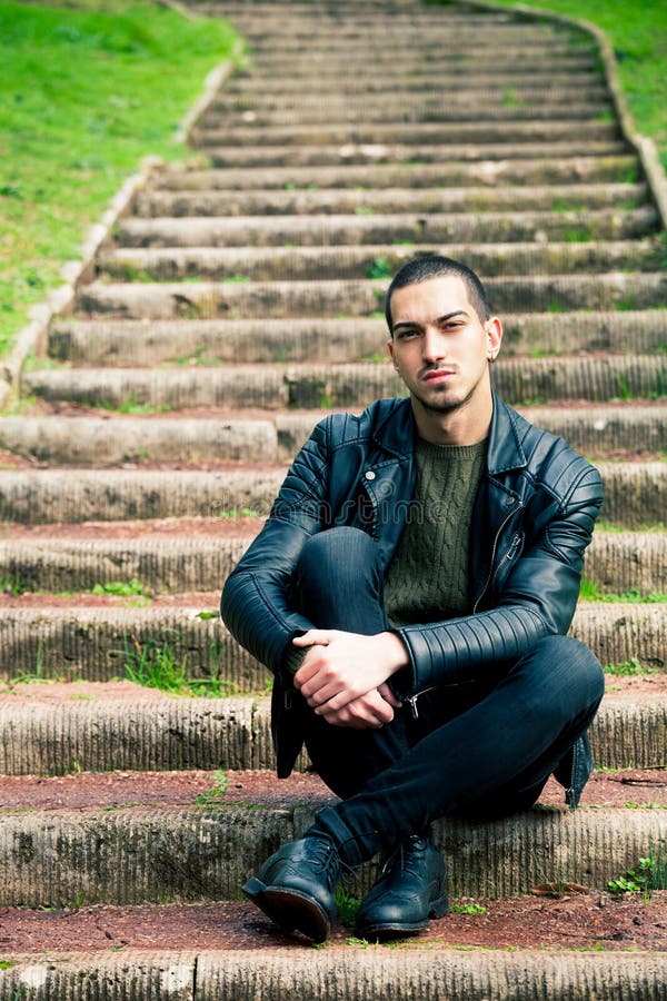 Handsome young man sitting on steps outdoors.