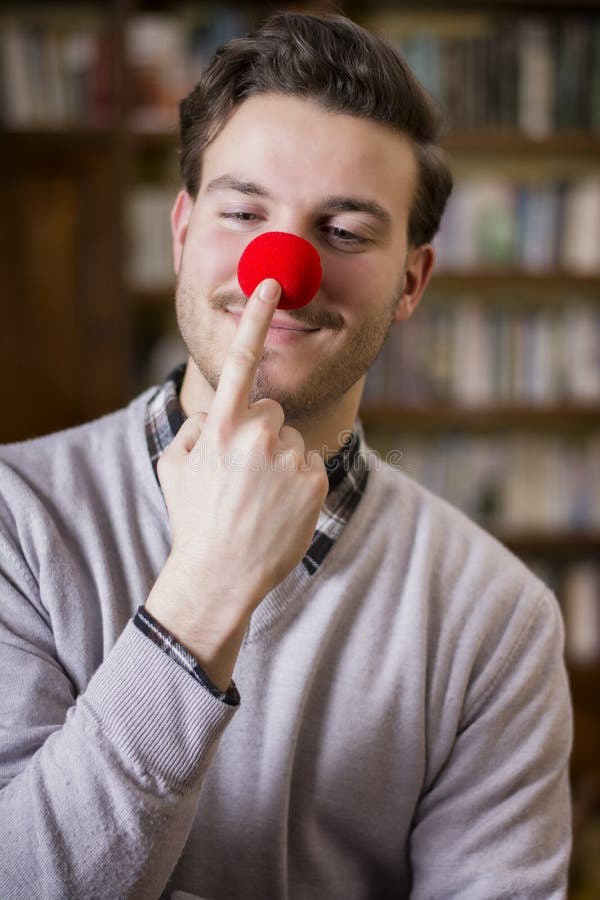 Handsome young man smiling and touching red clown nose