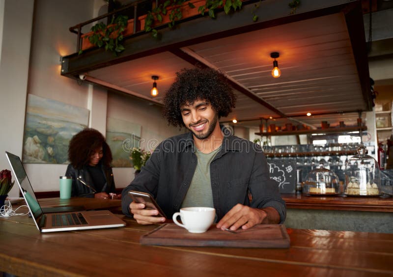 Handsome young man using smartphone and laptop in modern cafe while drinking coffee stock photo