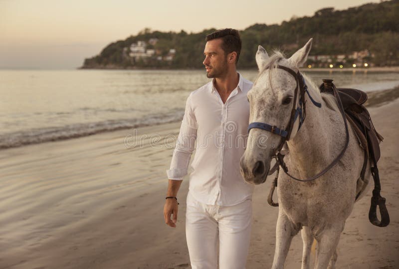 Handsome, young man walking with a stallion alongside the coast