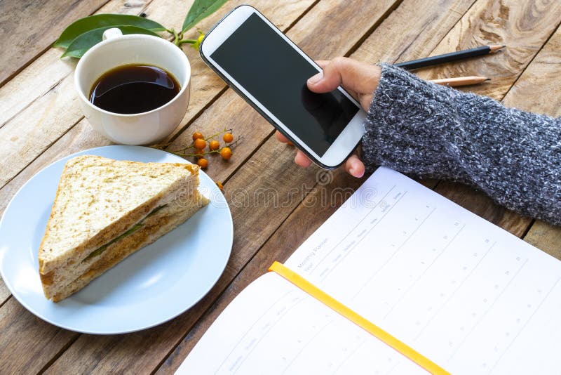 Handtag av kvinnor som har mobiltelefon med en bärbar dator för affärsarbete och frukost, snabbkaffe, smörgås royaltyfria bilder Handtag av kvinnor som har mobiltelefon med en bärbar dator för affärsarbete och frukost, snabbkaffe, smörgås royaltyfria bilder