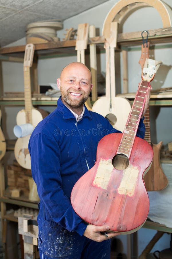 Handwerker, der unfertige Gitarre hält lizenzfreies stockbild Handwerker, der unfertige Gitarre hält lizenzfreies stockbild