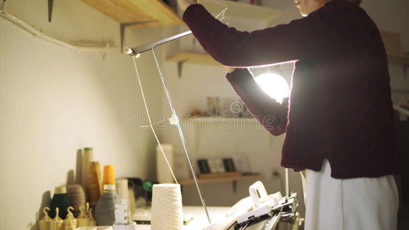 Handwerksfrau, die Thread in der Strickmaschine steht auf Tabelle in der Werkstatt zieht