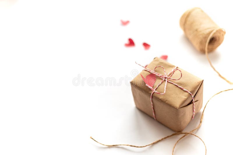 Handwerksgeschenkbox, die Bogen mit Hanfseil auf weißen vorgewählten Fokusroten kleinen Papierherzen bindet. Pakete eingewickelt im Kraftpapier gebunden mit Jutefaser auf whte Hintergrund, gerichtet auf Geschenk, vorgewählte Fokusrote kleine Papierherzen