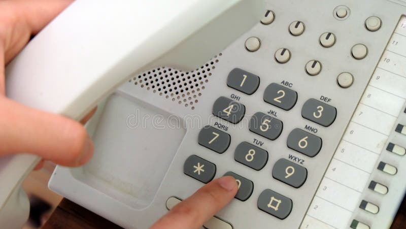 Finger dialing an office dial phone with many buttons when another hand is holding the receiver. Finger dialing an office dial phone with many buttons when another hand is holding the receiver.