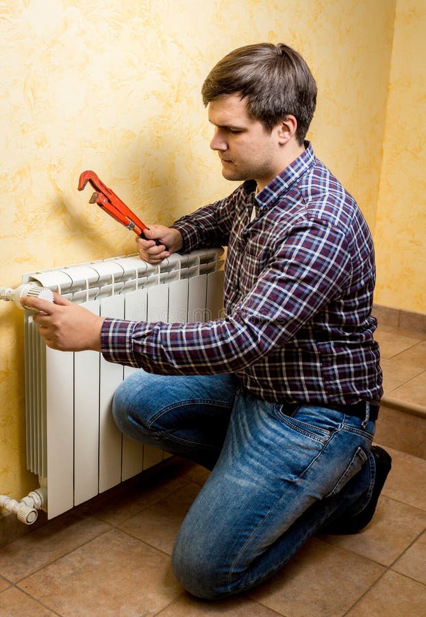 Handyman fixing heating radiator with red plumber pliers stock photography