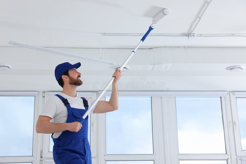 Handyman Painting Ceiling with Roller in Room, Back View Stock Photo
