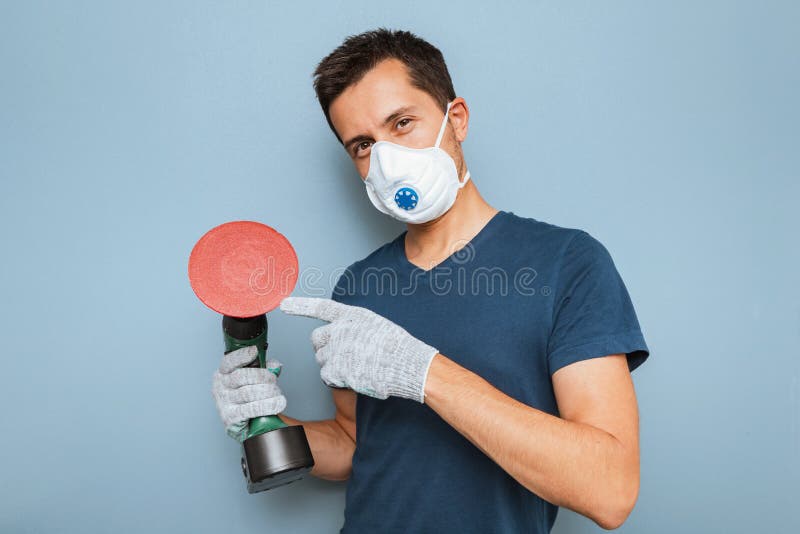 Handyman wearing respirator grinding wall with disc sanding machine. Worker labor and business concept royalty free stock image