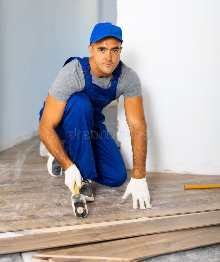 Handyman Worker in Work Clothes Use Rubber Hammers Installing Laminate
