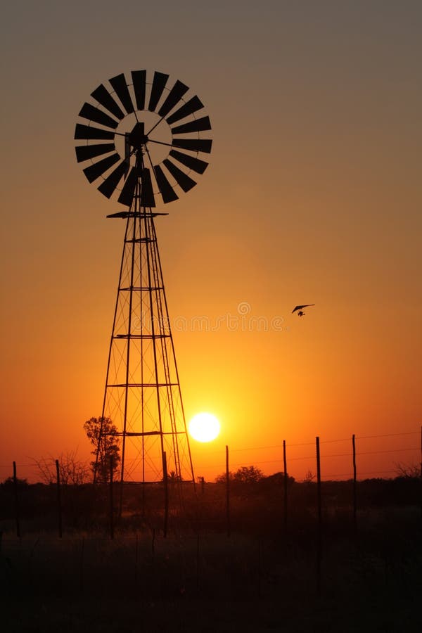 An hang glider flies in the sunset in the Namibian kalahari desert. In the frame there's a wind mill to pump water. An hang glider flies in the sunset in the Namibian kalahari desert. In the frame there's a wind mill to pump water.