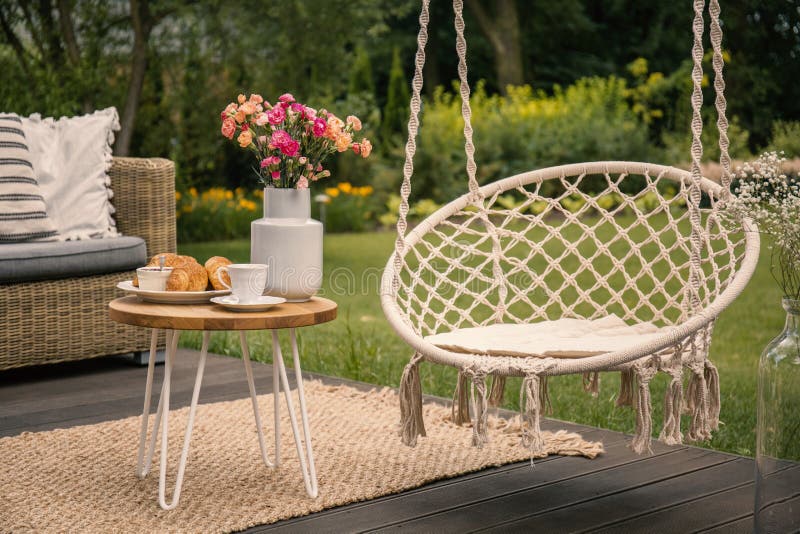 Hangende stoel naast lijst met bloemen op terras in de tuin tijdens de lente Echte foto stock fotografie Hangende stoel naast lijst met bloemen op terras in de tuin tijdens de lente Echte foto stock fotografie