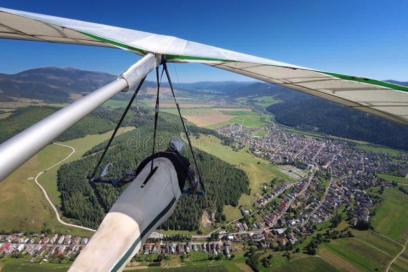 Pilot rogalu letí nad městečkem v alpském údolí