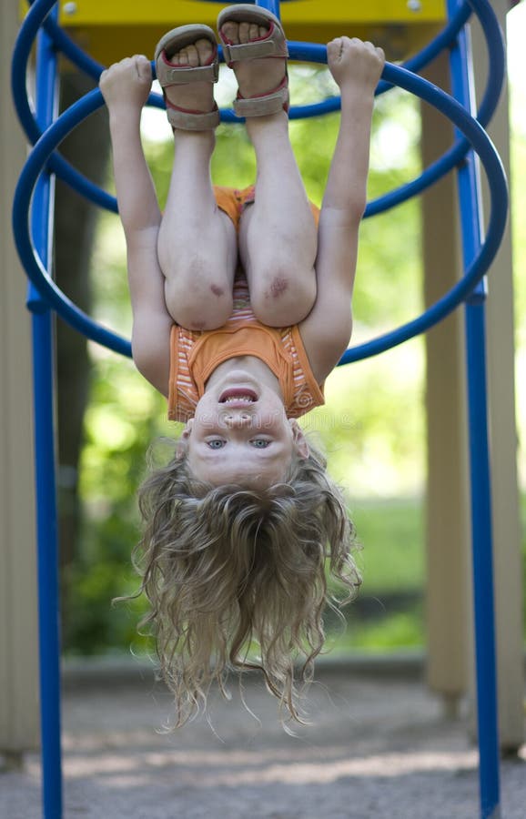 Young girl hanging upside down on the monkey bars.