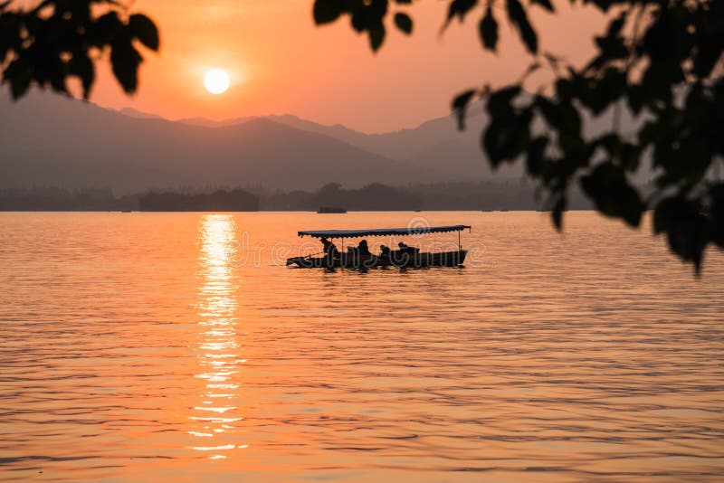 Hangzhou, China - November 9 2019: Beautiful sunset by the West Lake, a boat sailing on the lake with tourists