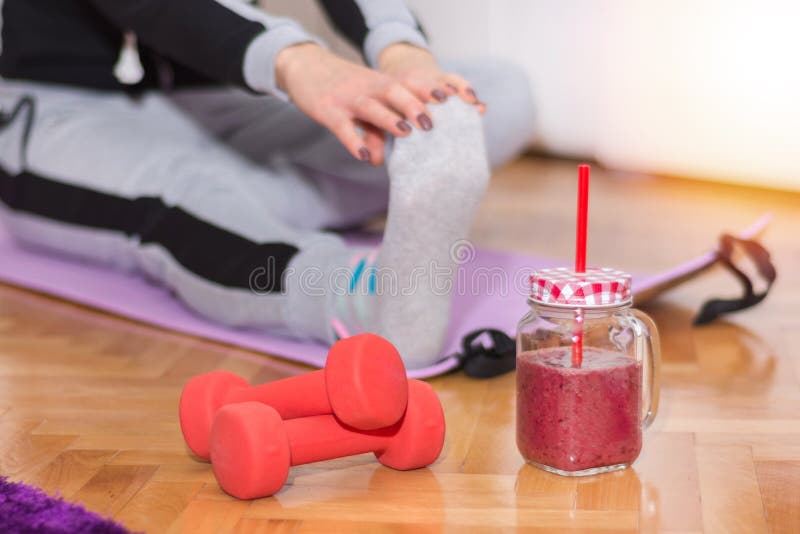 Hantel och smoothie i retro krus på golv och kvinnan som arbetar sträcka övningsben arkivfoton Hantel och smoothie i retro krus på golv och kvinnan som arbetar sträcka övningsben arkivfoton