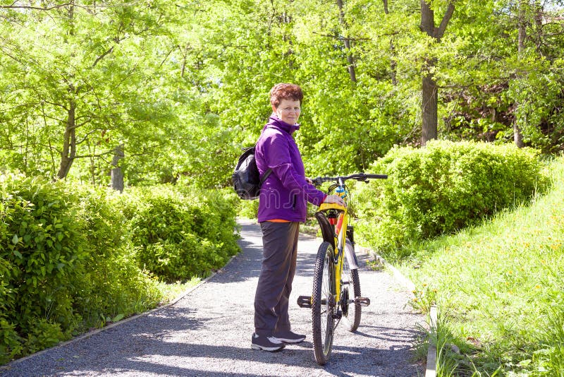 Happy adorable senior woman riding a bike in summer park