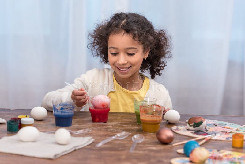 African american child painting easter eggs in glasses with paints