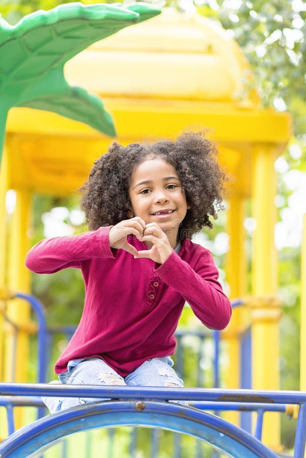 Happy African American Child playing in a park, girl making heart with her hands, love concept