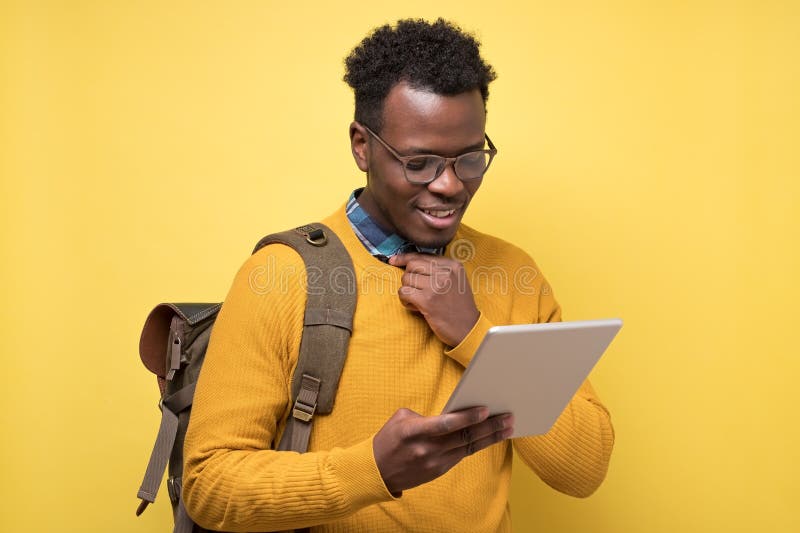Happy african american college student in glasses holding tablet on yellow wall. royalty free stock photography Happy african american college student in glasses holding tablet on yellow wall. royalty free stock photography