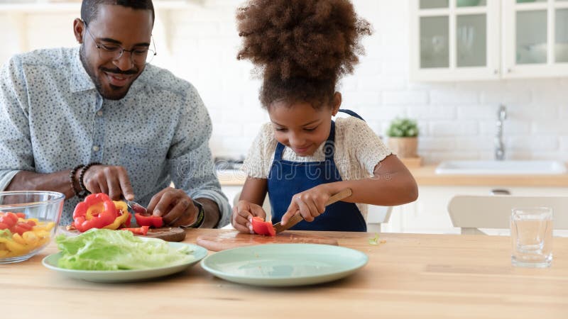 Happy African American daughter kid helping dad to prepare dinner