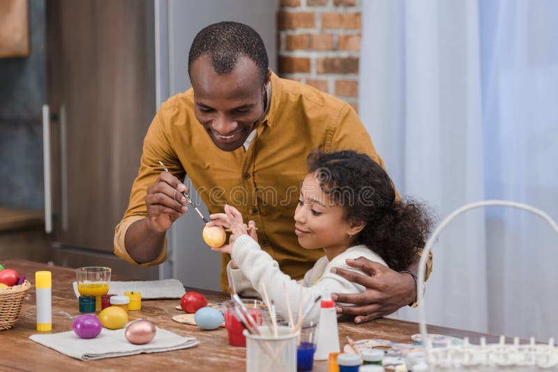 African american father and daughter painting easter eggs