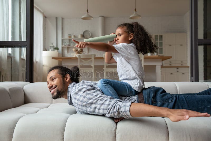 Happy African American girl sitting on father back, playing funny game stock image