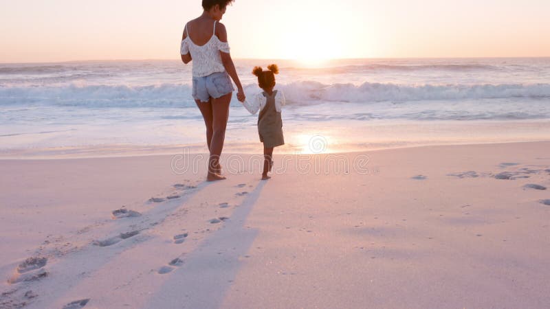 Black lovely mother and daughter walking on beach at sunset