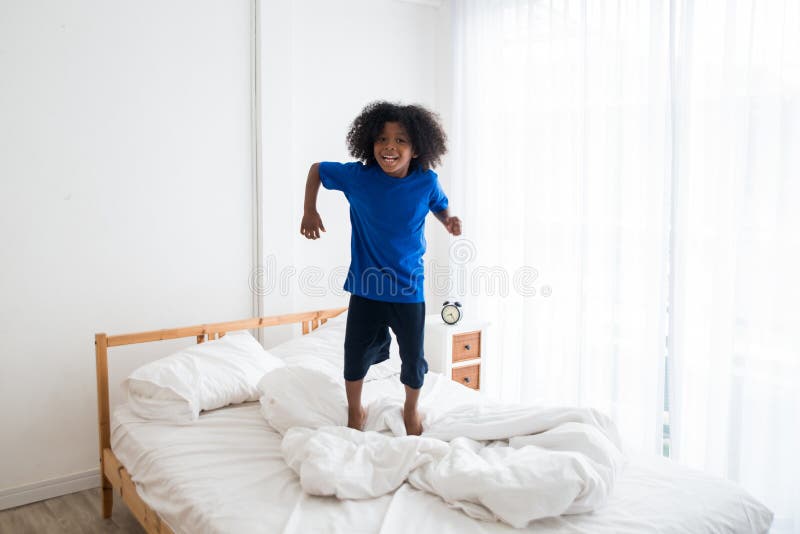 Happy African American naughty child jumping on the bed with happiness