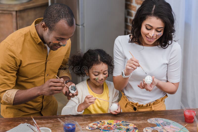 African american parents and daughter painting easter eggs