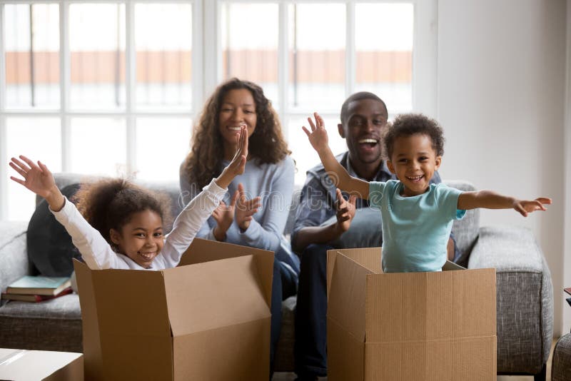 Happy african parents and kids playing in boxes enjoy relocation