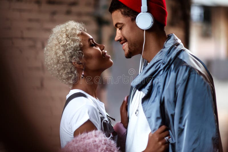 Happy Afro American man in heaphones and his dark skinned female with curly hairdo stand close to each other, look stock image Happy Afro American man in heaphones and his dark skinned female with curly hairdo stand close to each other, look stock image