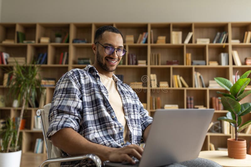 Happy arab male freelancer working on pc laptop, sitting in armchair at home interior, copy space royalty free stock photos