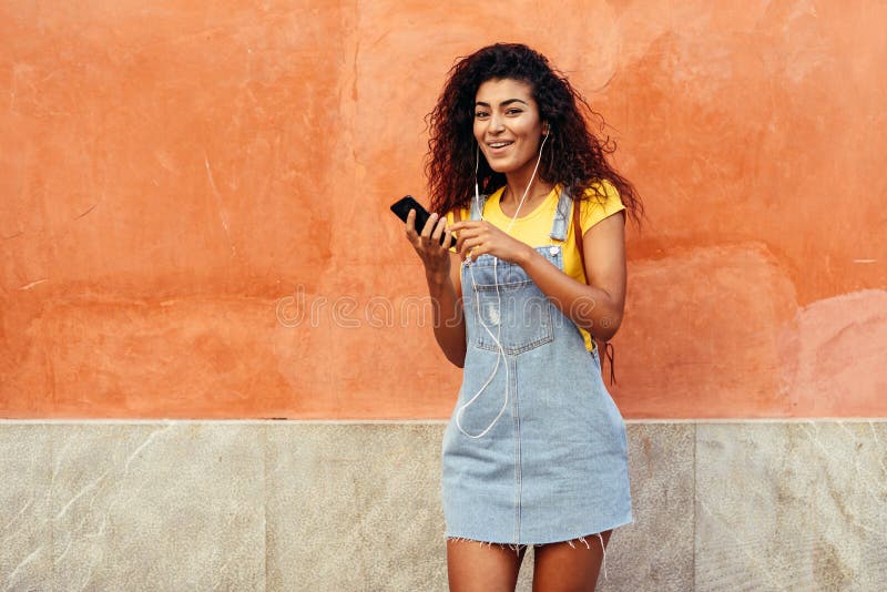 Happy Arab woman listening to music with earphones against red wall stock photo Happy Arab woman listening to music with earphones against red wall stock photo