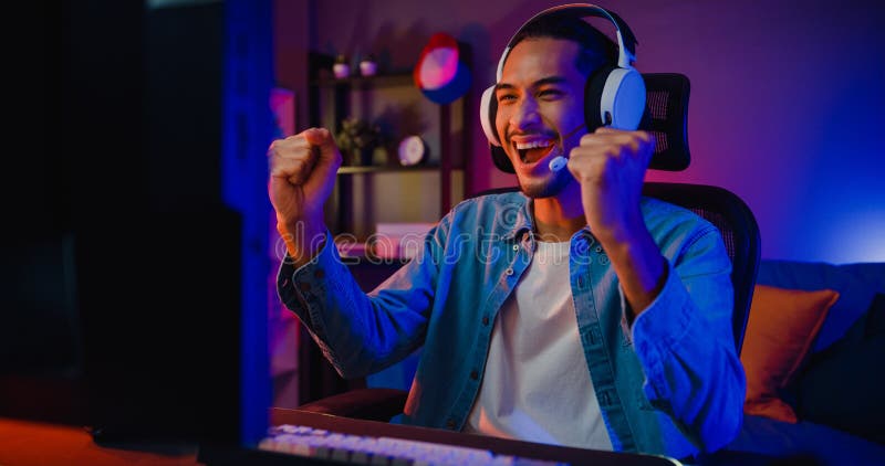 Happy asia girl gamer wear headphone competition play video game online  with smartphone colorful neon lights in living room at home. Esport  streaming game online, Home quarantine activity concept. Stock Photo