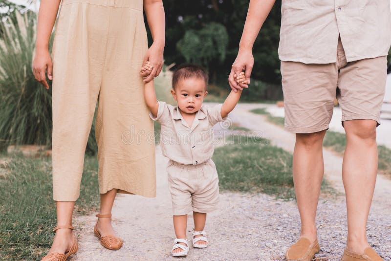 Happy asian baby boy learning to walk first steps with mother and father help at outdoor