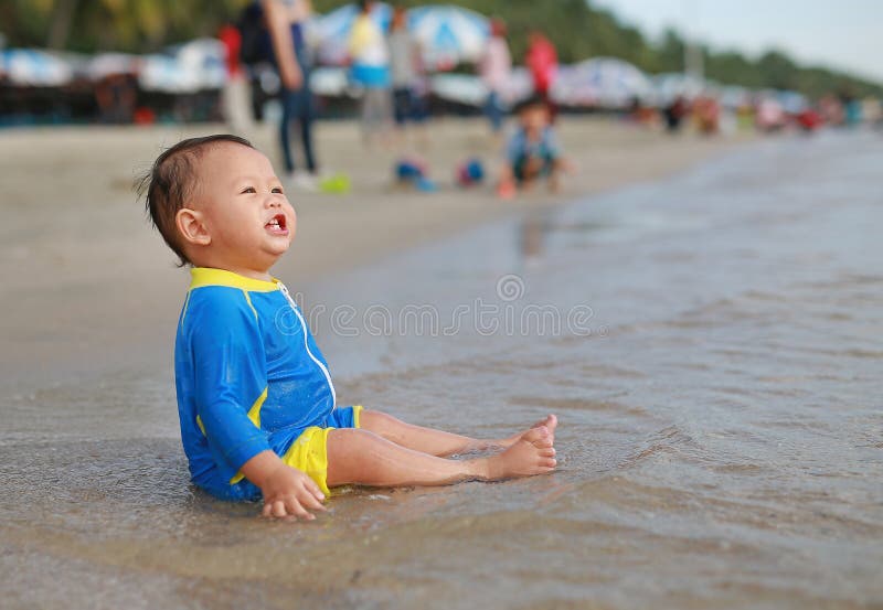 Happy of Asian baby boy in swimming suit sitting on the sand beach