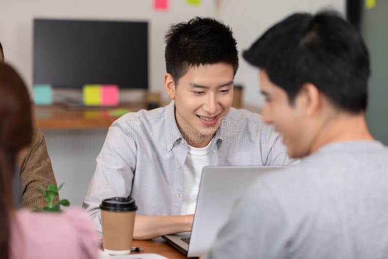 Happy Asian business young man smile and working with laptop and their team in co-working space or modern office