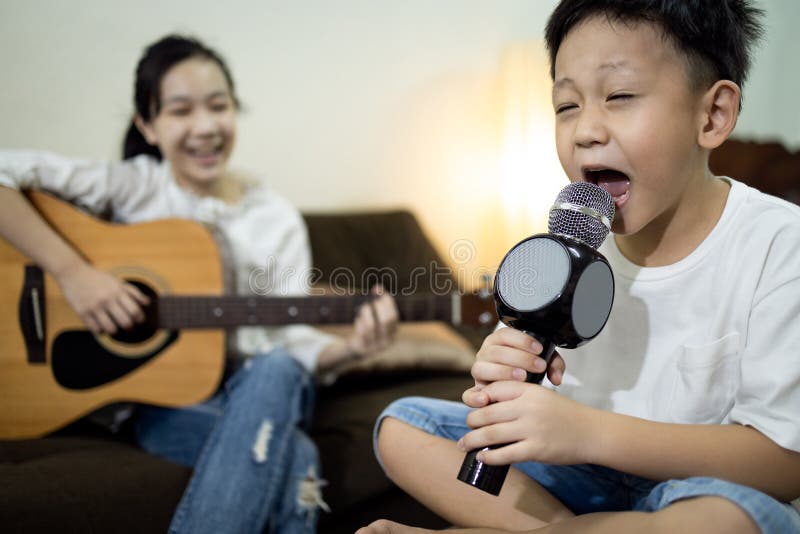 Happy asian child girl,kid boy singing a song together at home,family concert,sister plays the guitar,little brother hold a