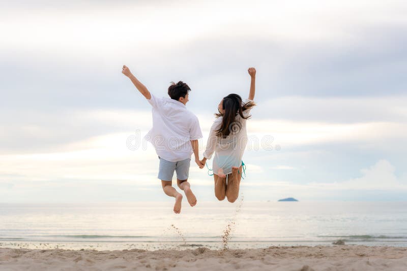 Happy Asian couple tourists jumping on beach vacations. Travel concept of young couple cheering for summer holidays showing