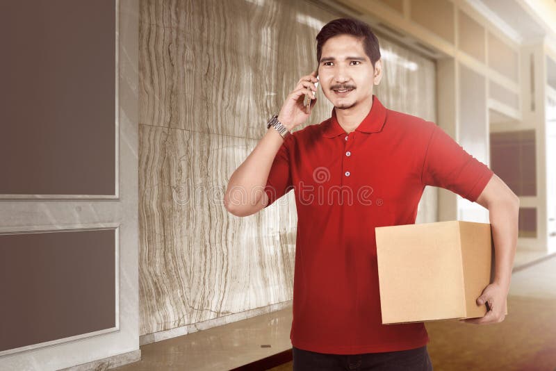 Happy Asian Delivery Man with Parcel Using Cellphone Stock Photo