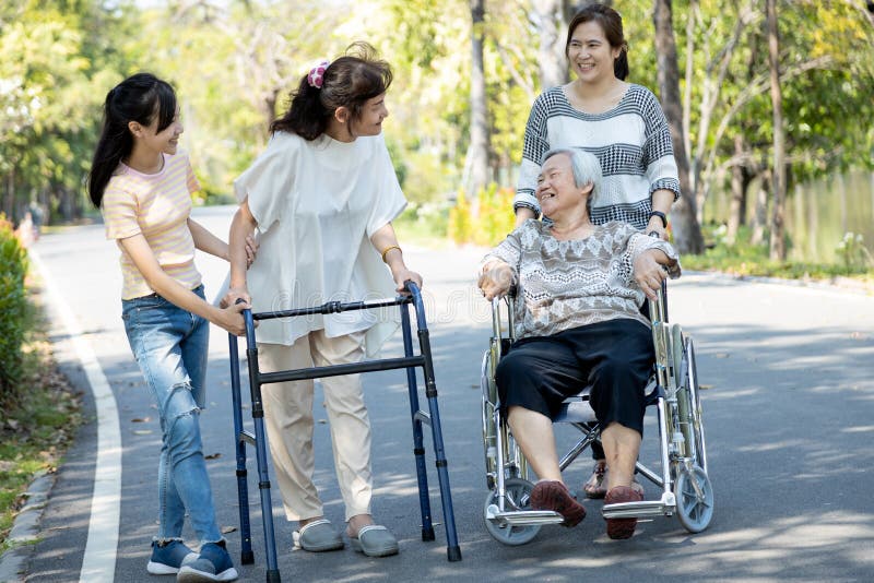 Happy asian family,senior woman, disabled grandmother with walker and wheelchair, daughter,teen granddaughter enjoying a walk in stock photos Happy asian family,senior woman, disabled grandmother with walker and wheelchair, daughter,teen granddaughter enjoying a walk in stock photos